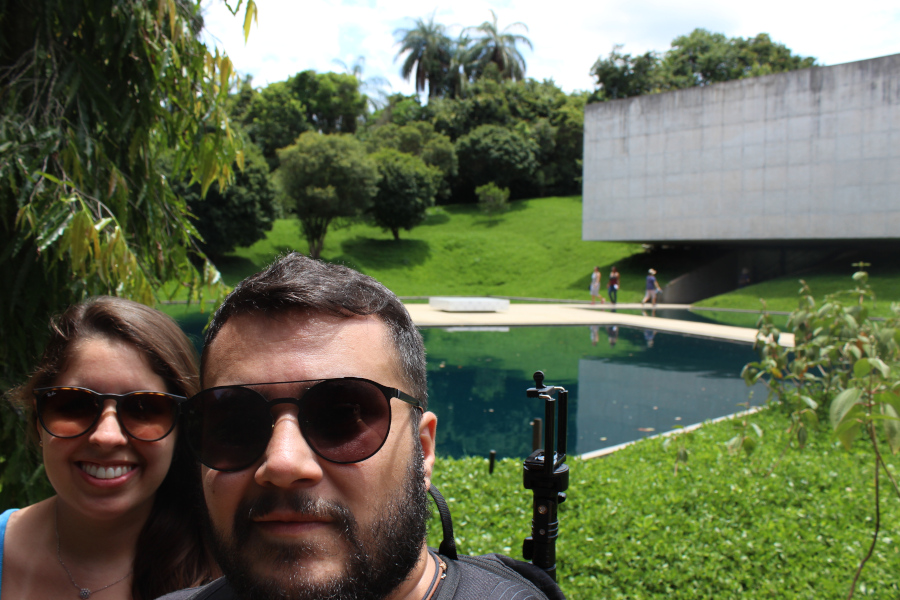 Chrys e seu marido, Thiago, num templo budista com um grande buda amarelo ao fundo em Belo Horizonte.